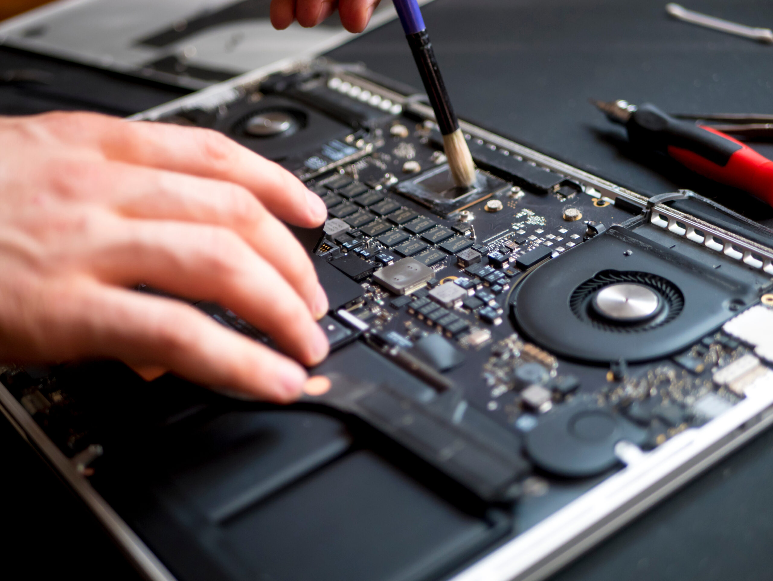 hand with brush clearing the disassembled laptop from dust and dirty close up in workshop